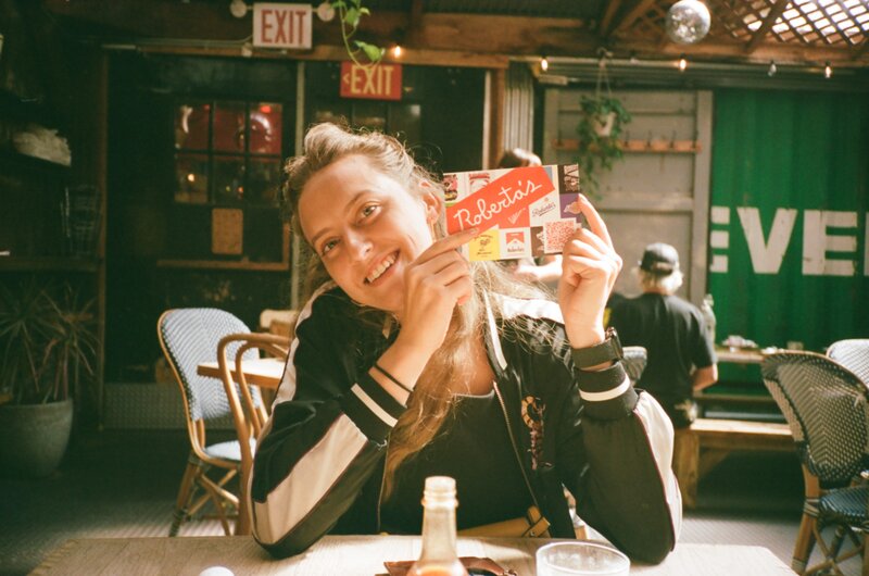 A women holding up a postcard at a pizza place called Roberta's in Brooklyn, NY.