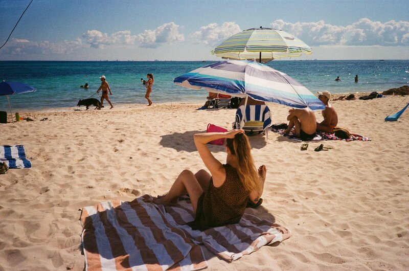 A beautiful beach in Mexico with a woman finding some shade under an umbrella